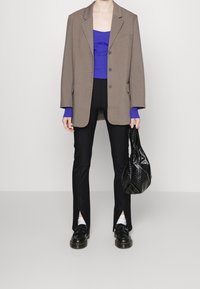 Brązowa, oversize'owa marynarka na purpurowej bluzce, w komplecie z czarnymi spodniami z bocznymi rozcięciami, czarnymi butami oraz fakturowaną czarną torebką.