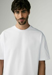 Tricou alb din bumbac cu guler rotund, mâneci scurte și o croială lejeră, având un material moale și o textură netedă.