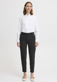 Witte overhemdd met lange mouwen, gecombineerd met donkergrijze op maat gemaakte broek. Glad stof met een subtiel patroon, taps toelopende broekspijpen. Beige schoenen.