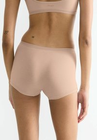 Beige Boyshorts aus weichem, dehnbarem Material mit einem tief sitzenden Design. Sie verfügen über einen glatten Bund, keine sichtbaren Nähte und ein minimalistisches Logo.