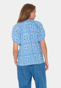 Blusa blu a fantasia con maniche a sbuffo, caratterizzata da un design floreale e un tessuto testurizzato. Abbinata a jeans azzurri a vestibilità rilassata.