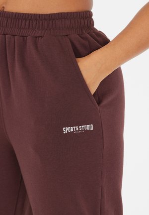 Burgundy sweatpants with an elastic waistband, side pockets, and the text "SPORTS STUDIO ATHLETICA" printed in white on the left thigh.