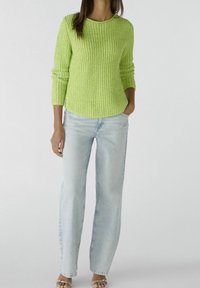 Limegrøn, ribbestrikket sweatshirt med lange ærmer, parret med lyseblå straight-leg jeans og gennemsigtige hælsandaler.