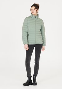 Lysegrøn pufferjakke med vandret syninger, høj krave og lynlås. Sammen med sorte skinny jeans og kraftige sorte støvler.