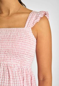 Rosa rutig klänning med smockad livstycke, volangärmar och flödande tyg, vilket framhäver mjuk textur och ljus färg.