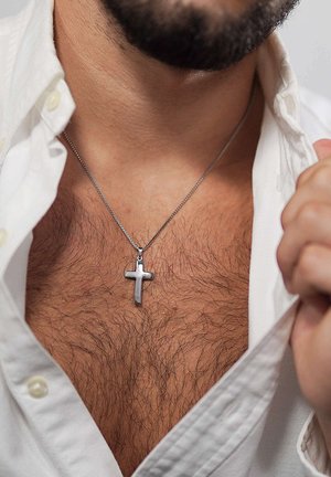 Mann trägt ein teilweise aufgeknöpftes weißes Hemd, das Brusthaare und eine silberne Kreuzanhängerkette zeigt.