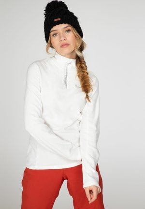 Pullover in pile bianco con colletto a zip quarti, caratterizzato da un sottile dettaglio del logo e una consistenza morbida. Abbinato a pantaloni rossi e un berretto di maglia nera.