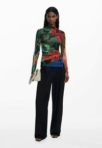 Bluzka z długim rękawem wykonana z mieszanych tkanin, ozdobiona kwiatowymi i geometrycznymi wzorami, zestawiona z czarnymi, szerokimi spodniami z wysokim stanem. Uzupełniona białą torebką.