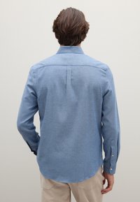 Camicia azzurro chiaro con bottoni, realizzata in tessuto strutturato, con maniche lunghe, colletto e orlo curvo nella parte inferiore.