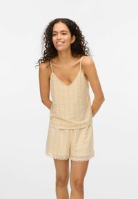 Lys beige blonde sæt med en ærmeløs top med V-hals og matchende shorts, begge med blomster mønstre og bølgede kanter.