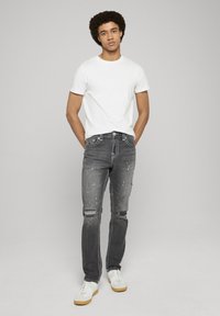 Grijze gescheurde spijkerbroeken met witte accenten, met een slim fit en een licht verweerde textuur, gecombineerd met een effen wit T-shirt en witte sneakers.