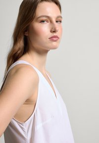 Weißes ärmelloses Oberteil mit tiefem V-Ausschnitt, aus einem glatten Stoff gefertigt, mit minimalen Nähten und einer lässigen Passform.