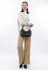 Black leather handbag with a smooth texture, featuring a curved shape and short strap. Worn with a light beige knitted sweater and tan trousers.