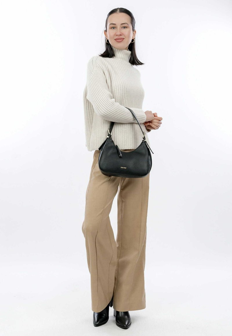 Black leather handbag with a smooth texture, featuring a curved shape and short strap. Worn with a light beige knitted sweater and tan trousers.