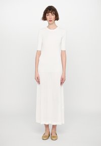Robe en tricot côtelé blanche avec des manches courtes, design fluide et longueur midi. Assortie à des ballerines dorées avec des accents à lanières.