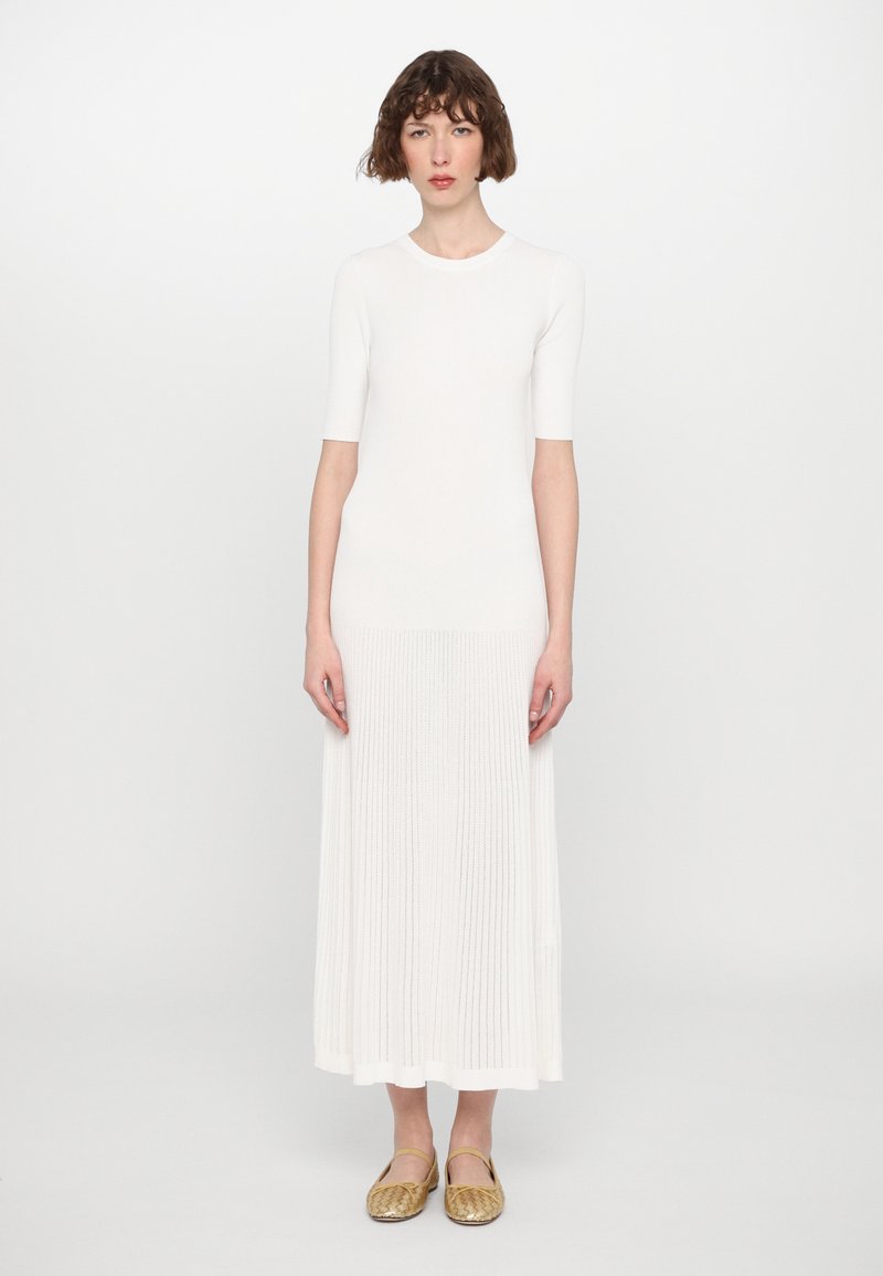 Robe en tricot côtelé blanche avec des manches courtes, design fluide et longueur midi. Assortie à des ballerines dorées avec des accents à lanières.