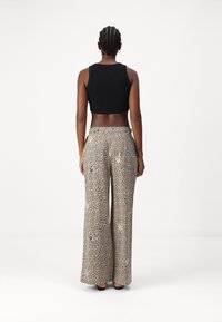 Schwarzes, kürzeres Tanktop kombiniert mit weit geschnittenen, beigen Leoprint-Hosen, die eine weiche Textur und einen elastischen Bund haben.