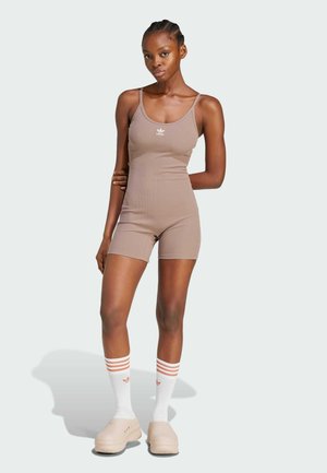Smeđi rebrasti bodysuit s tankim naramenicama, bijeli Adidas logo i matching čarape s narančastim prugama, uparen s bež cipelama.