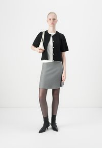 Black knitted short-sleeve cardigan with white buttons, layered over a white top. Grey skirt, sheer black tights, and black pointed ankle boots.