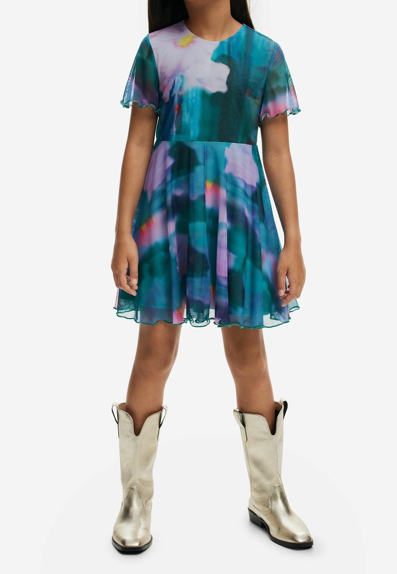 Sukienka w kwiaty w kolorze turkusowym i fioletowym, z krótkimi rękawami i falbaniastymi brzegami, w zestawie z metalicznymi srebrnymi kowbojkami.