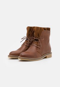 Brune skinn ankel støvler med semsket detaljer, snøringsdesign, teksturert overflate, lys brun såle og tonale sømmer på sidene.