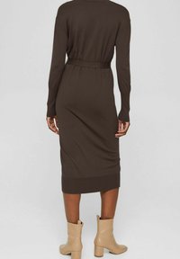 Brązowa dzianinowa sukienka z długimi rękawami, paskiem w talii i żeberkowym wykończeniem. Połączona z beżowymi botkami za kostkę o gładkiej, dopasowanej fakturze.