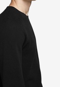Pull noir texturé à col rond avec un motif côtelé subtil, coupe ajustée, sans ornements ni graphiques apparents.