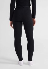 Zwarte leggings gemaakt van rekbaar materiaal, met een hoge tailleband, een gladde textuur en een aansluitend ontwerp, gezien vanuit de achterkant.