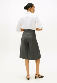 Culottes gris a rayas hechas de tela sastre, con una cintura alta, bolsillos laterales, y combinados con una camisa blanca de cuello y tacones negros.