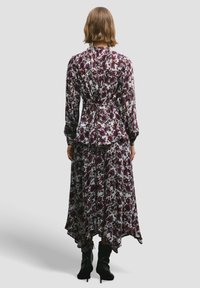 Abito lungo a fiori con maniche lunghe, in tessuto bianco e bordeaux, con vita increspata e orlo asimmetrico, abbinato a stivaletti neri alla caviglia.