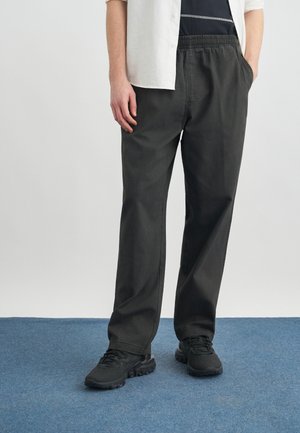 Személy laza fekete nadrágot visel gumis derékrésszel, fekete tornacipővel, tengerészkék pólóval és fehér, felhajtott ujjú inggel.