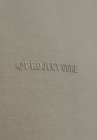Bežinė medžiaga su minkšta tekstūra, kuri turi įspaustą „©PROJECT CORE“ logotipą šiek tiek tamsesnėje spalvoje.