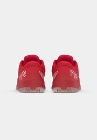 Baskets de sport rouges avec une tige texturée, un col rembourré et une semelle en caoutchouc. Logo TYR distinctif et accents de design d'aile sur les côtés.