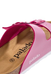 Infradito rosa con tomaia in pelle, soletta in sughero, cinturino regolabile con fibbia e soletta testurizzata. Nome del marchio visibile all'interno.