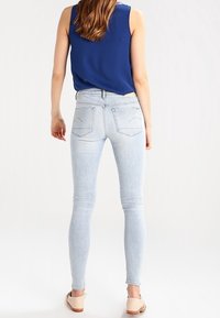 Vaqueros ajustados de color azul claro, confeccionados en denim, con una cintura de altura media, bolsillos traseros estándar y una textura suave, ligeramente desgastada.