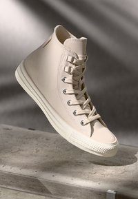 Baskets montantes en cuir beige avec des lacets ton sur ton, semelle en caoutchouc et capuchon de toe texturé avec un motif en losange.