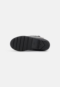 Semelle de sneaker noire en matériau en caoutchouc texturé, avec des rainures profondes pour la traction et un motif en chevron subtil.