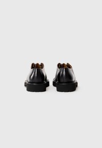 Black leather shoes with a textured finish, featuring a chunky black sole and brown leather lining, showcasing a rounded back design.