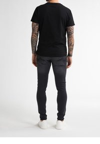 Black crew neck t-shirt, short sleeves, paired with dark gray slim-fit jeans and white sneakers. Visible tattoos on arms.