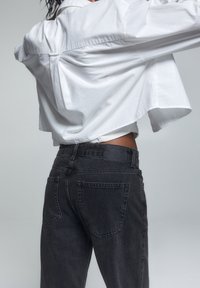 Camicia bianca corta con bottoni, dal fit ampio, abbinata a jeans in denim neri a vita alta con tasche posteriori e una leggera sfumatura.