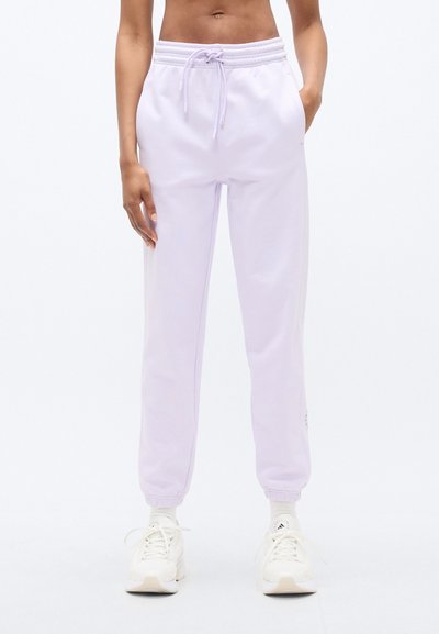 Pantalon de survêtement lilas en tissu doux, doté d'une ceinture élastique avec cordon de serrage, chevilles resserrées et poches latérales. Détail du logo visible.