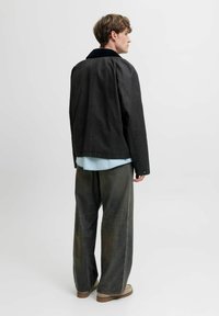 Czarna kurtka z kontrastującym ciemnym kołnierzem, w połączeniu z szerokimi, lekko zniszczonymi szarymi dżinsami i beżowymi butami. Ubranie wygląda na swobodne i luźne.