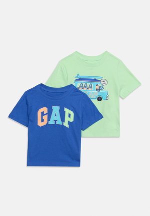 Deux t-shirts à manches courtes pour tout-petits, un bleu avec des lettres colorées "GAP", un vert clair avec un graphique de bus et de planches de surf indiquant "Surf's up!"