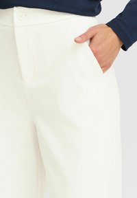 Pantalons blancs ajustés avec une texture lisse, dotés d'une poche latérale et d'une simple fermeture à bouton au niveau de la taille.