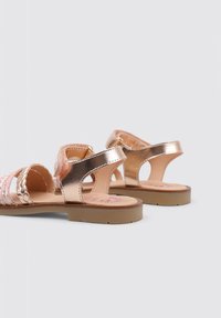Sandalias de color oro rosa con tiras trenzadas, plantilla suave y suela de goma. Presenta lados abiertos y correas ajustables en el tobillo.