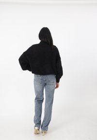 Zwarte gebreide cropped trui met een hoge hals, gedragen met lichtblauwe spijkerbroeken met rechte pijpen. Het model draagt beige hoge hakken.
