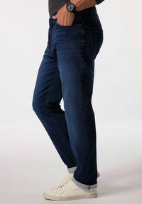 Jeans de mezclilla azul oscuro con corte recto, que cuentan con bolsillos delanteros, un bolsillo trasero y dobladillos con vuelta. Combinados con zapatillas blancas.