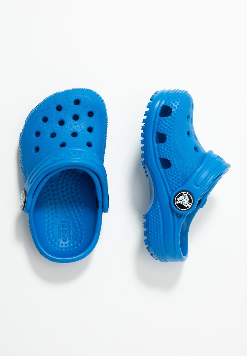Paire de sabots bleus à enfiler avec des trous de ventilation et des sangles arrière réglables, présentée en vues de dessus et de côté sur fond blanc.