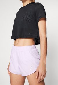 Musta lyhythihainen urheilupaita, jossa on rei'itetty kuvio, yhdistettynä vaaleanlaventelivärisiin shortseihin, joissa on joustava vyötärö ja heijastava logo.