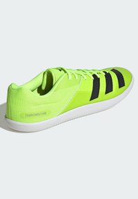 Limetkovozelená športová topánka s čiernymi akcentmi, textúrovaný sieťovaný zvršok, šnurovanie a biela gumová podrážka. Má branding na päte.